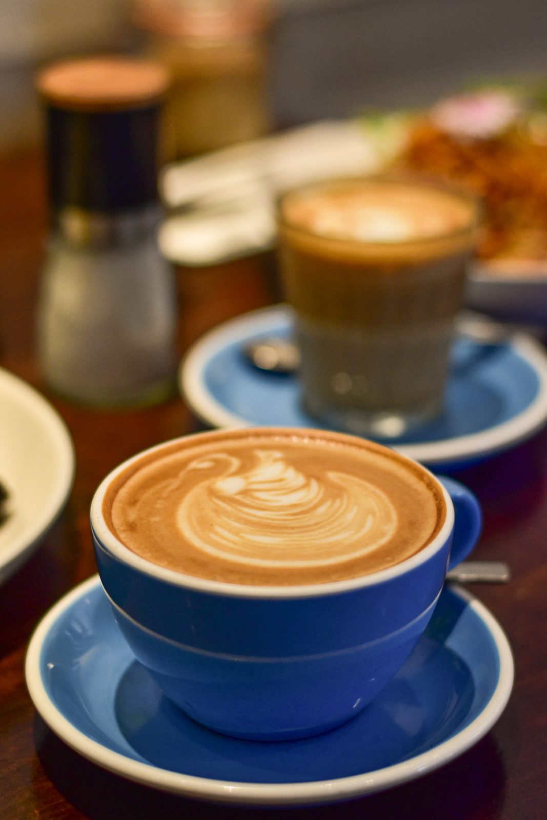 Latte art on a flat white at Mission Bay Cafe, with a second coffee and brunch plate behind it